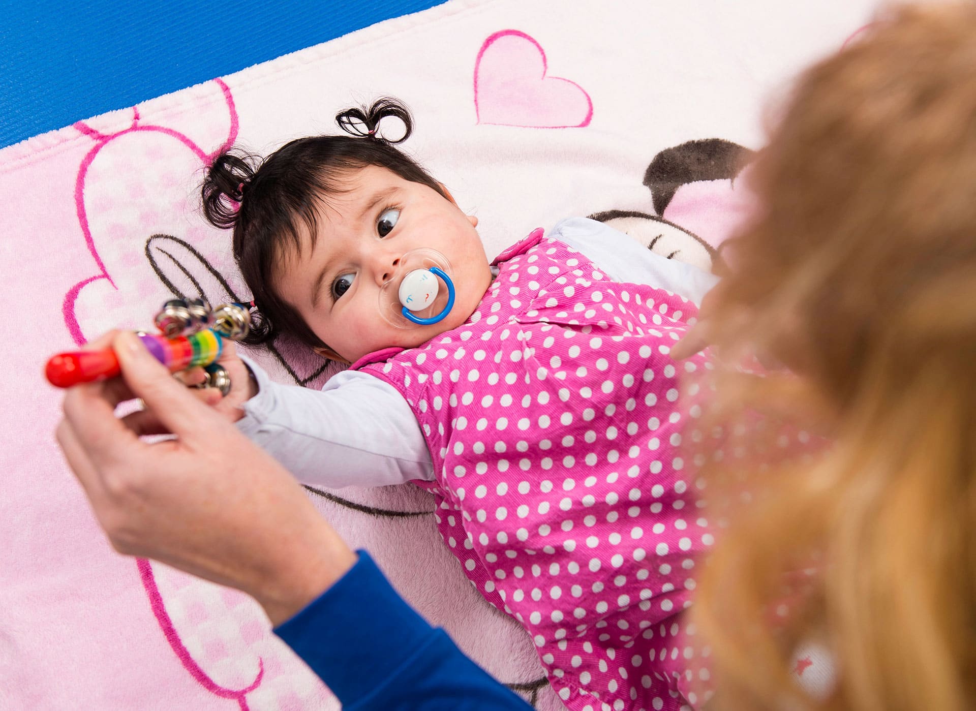 Baby op een speelkleed tijdens een behandeling kinderfysiotherapie, met een rammelaar als afleiding.