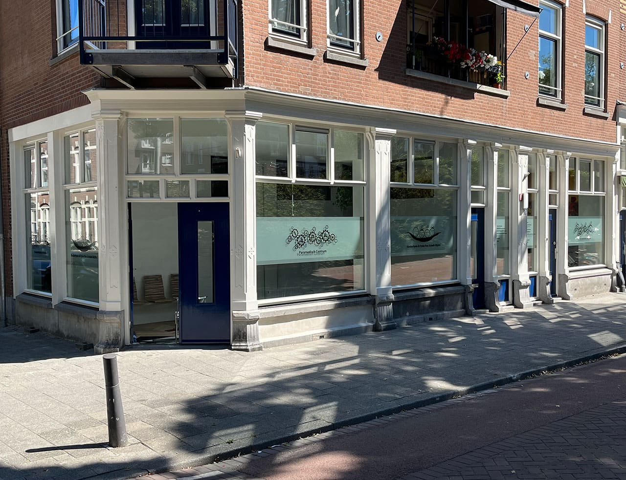 De hoekpand van het Paramedisch Centrum aan de Oostzeedijk Beneden in Rotterdam Kralingen, met grote ramen en een blauwe voordeur.